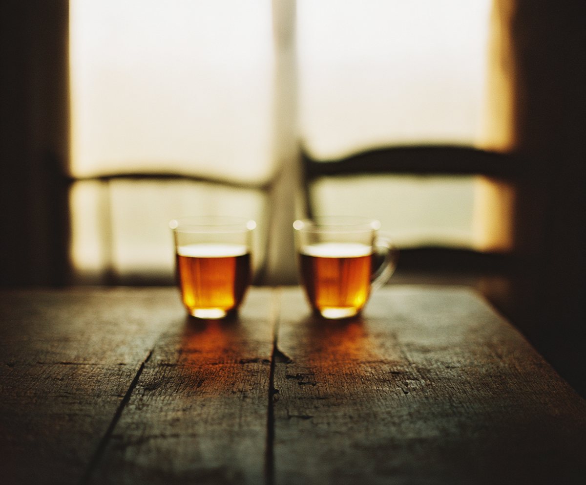 Two glasses of tea on a wooden table beside a window at dusk